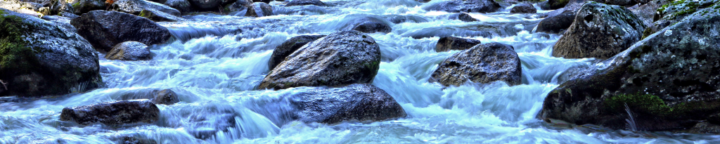 Rushing water flowing over river rocks and boulders, illustrating the natural environmental flows needed to sustain aquatic ecosystems.
